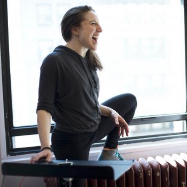 Ephrat Asherie, a thirty-something white woman laughing during a rehearsal with one foot up on a radiator.